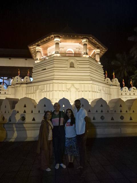       Night-time portrait of travellers in front of the illuminated Temple of the Tooth in Kandy.
  