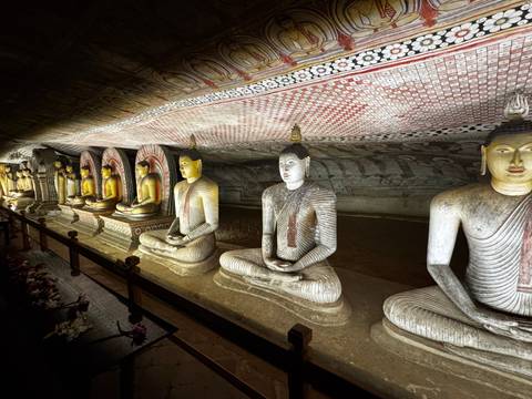       Row of illuminated Buddha statues lines the richly painted interior of Dambulla Cave Temple.
  