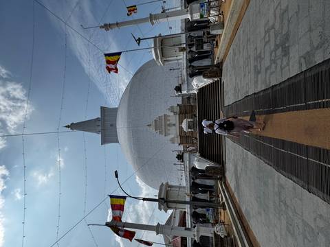       Visitors walk up a carpeted stairway toward the towering white stupa of Ruwanwelisaya under blue skies.
  