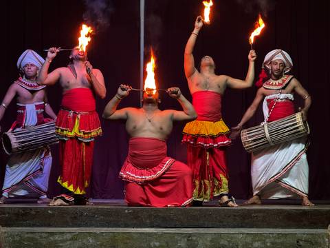       Traditional Sri Lankan fire dancers perform on stage wearing vibrant red and white costumes.
  