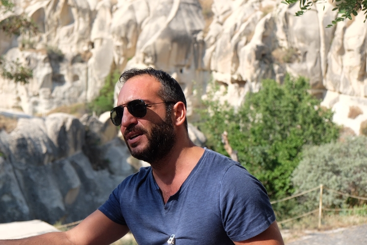 Man in sunglasses with rocky background in a sunny setting.