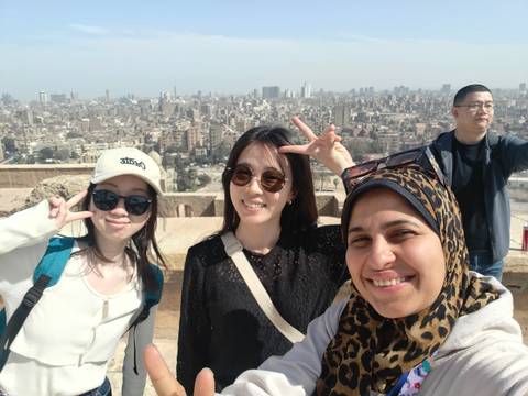       Selfie of friends flashing peace signs with sprawling Cairo skyline behind them.
  