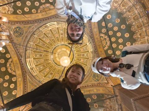       Three friends looking down at camera beneath an intricately painted mosque ceiling.
  