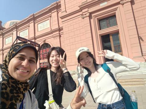       Guide and two tourists posing outside the pink-stone Egyptian Museum in Cairo.
  
