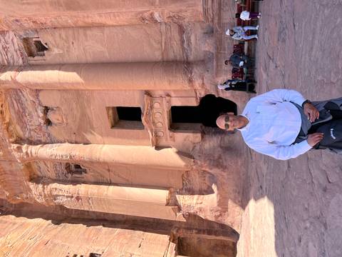      Man smiling in front of a carved sandstone facade at Petra with warm afternoon light.
  