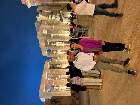       Couple standing among illuminated columns and statues in Luxor Temple at night.
  