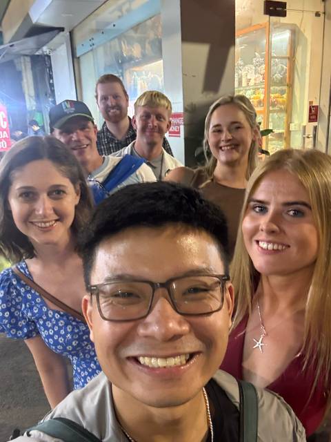       Casual nighttime selfie of smiling young travelers crowded together on a busy street.
  