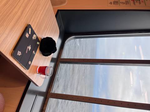       Cozy ferry cabin table with laptop, plush hat, and glass of red tea overlooking the open sea.
  