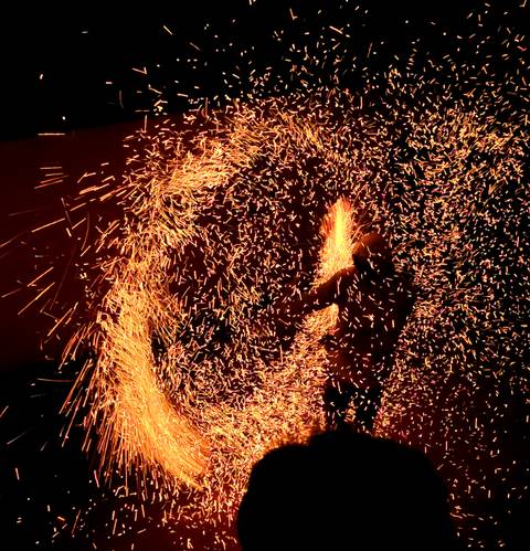       Performer spins fire, creating a dramatic swirl of golden sparks against the night sky.
  