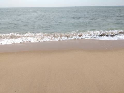       Gentle wave laps onto a quiet sandy beach under an overcast sky.
  