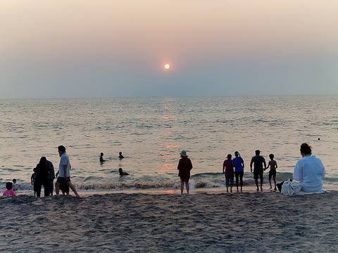       People wade and watch the sun set over the Arabian Sea from a sandy Kerala beach.
  