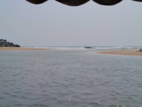       Calm estuary where river meets the Arabian Sea under a hazy grey sky.
  