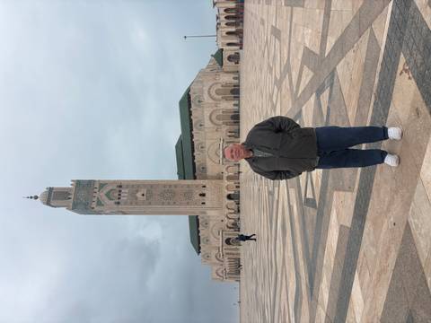       Visitor stands before the grand Hassan II Mosque with its soaring minaret under cloudy skies.
  
