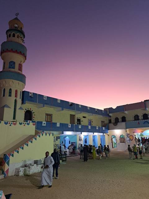       Colorful Nubian guesthouse courtyard glows under a violet twilight sky.
  