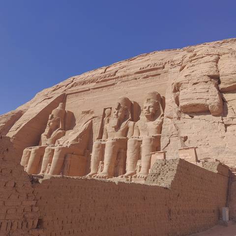       Massive seated statues of Pharaoh Ramses II carved into a sandstone cliff under a clear blue sky.
  