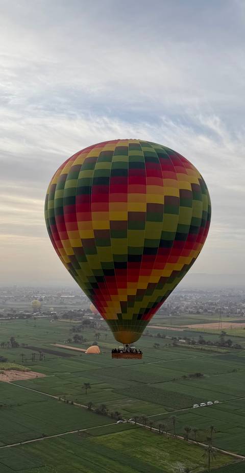       Colorful hot-air balloon floating above hazy landscape at dawn.
  