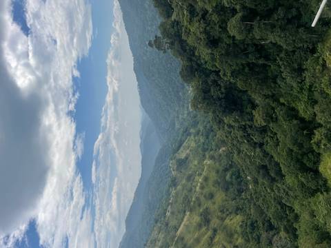       Expansive view of lush green valleys and distant misty mountains under partly cloudy sky.
  