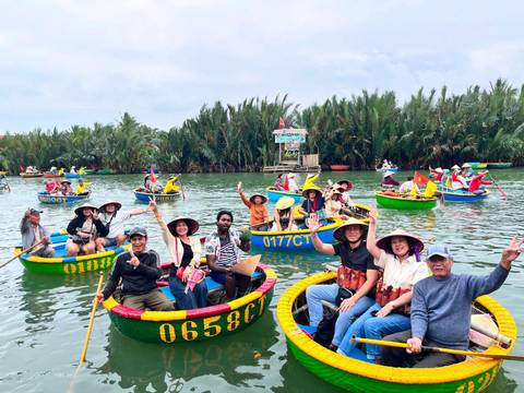       Dozens of tourists in brightly painted basket boats wave while floating on a palm-lined river.
  