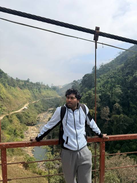      Traveler stands on a narrow suspension bridge spanning a misty forested valley.
  