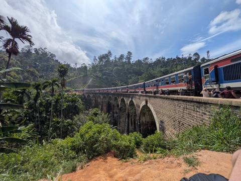       Long passenger train crossing the famous stone Nine Arches Bridge above a lush green valley.
  