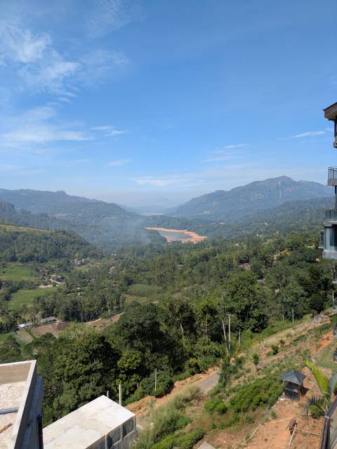       Panoramic view over a green mountain valley with a winding river and distant reservoirs under a blue sky.
  