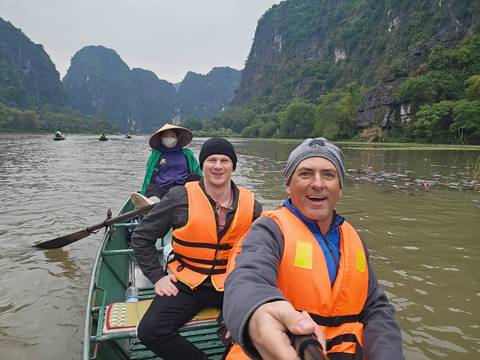       Selfie of travellers in life jackets rowing through limestone karst scenery of Ninh Binh.
  