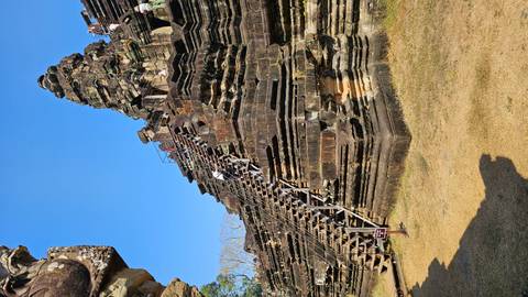       Visitors climb steep wooden stairs of an ancient Khmer temple pyramid.
  