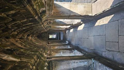       Long vaulted stone passageway inside an ancient Khmer temple lit by side windows.
  
