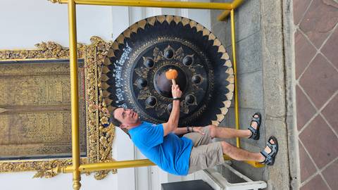       Tourist strikes a ceremonial gong outside a decorated Thai temple pavilion.
  