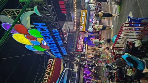       Neon night scene of Patong Beach sign with crowds, motorbikes and bars lighting up the street.
  