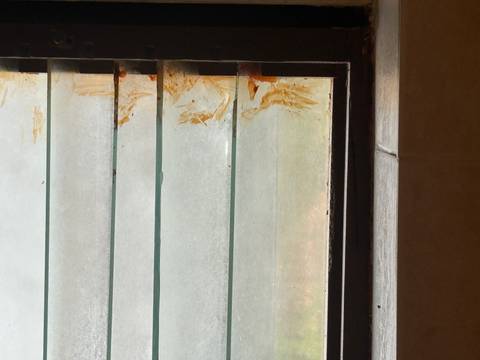       Bathroom louvre window with grime and rust-stained edges.
  