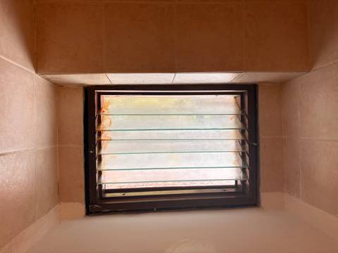       Small bathroom window with frosted glass and rust stains in tiled wall.
  