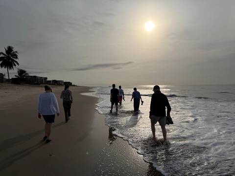       Travelers stroll along quiet beach shoreline in soft morning sunlight.
  