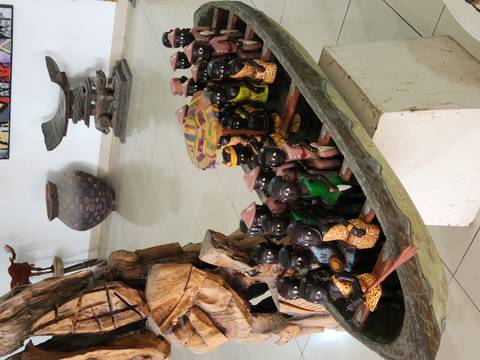       Close-up of an elaborate carved wooden boat filled with miniature human figurines displayed inside a gallery.
  