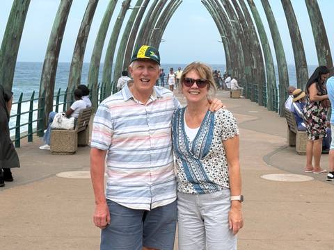       Smiling couple posing on a curving seaside pier with the Indian Ocean in the background.
  