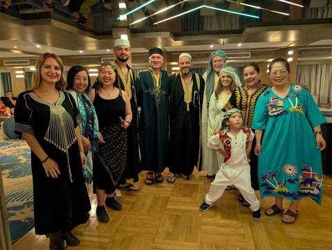       Group of guests dressed in traditional galabeya outfits smiling on a Nile cruise lounge.
  