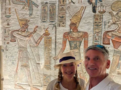       Selfie of two travellers standing before vivid wall reliefs inside an ancient Egyptian temple.
  