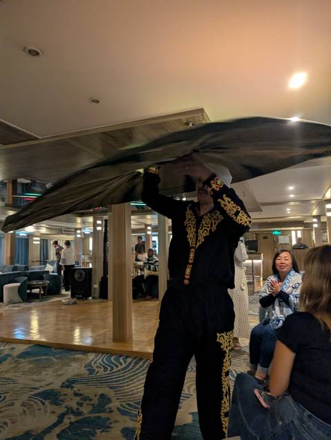       Entertainer in embroidered costume spinning a large Tanoura skirt inside a cruise lounge.
  