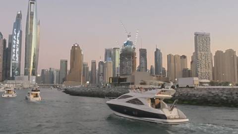       A sleek yacht cruises past the glittering skyscrapers of Dubai Marina at dusk.
  