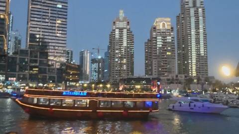       A traditional dhow adorned with neon lights glides through Dubai Marina after dark.
  
