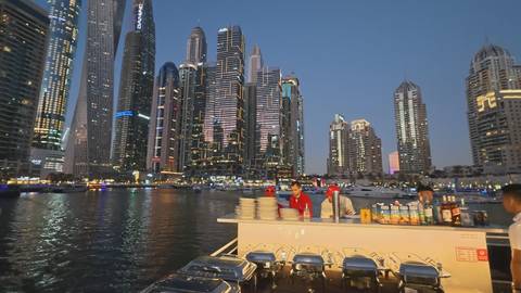       Evening buffet set up on a cruise boat with Dubai Marina’s illuminated skyscrapers in the background.
  