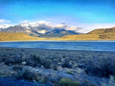       Expansive lake bordered by dry steppe with dramatic cloud-capped peaks of Torres del Paine in the distance.
  