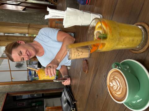       Smiling woman enjoying colorful iced drinks at a cozy café table.
  