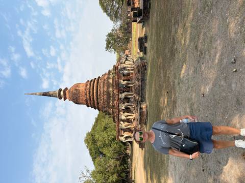       Traveler posing before an ancient brick stupa encircled by elephant statues in Sukhothai.
  