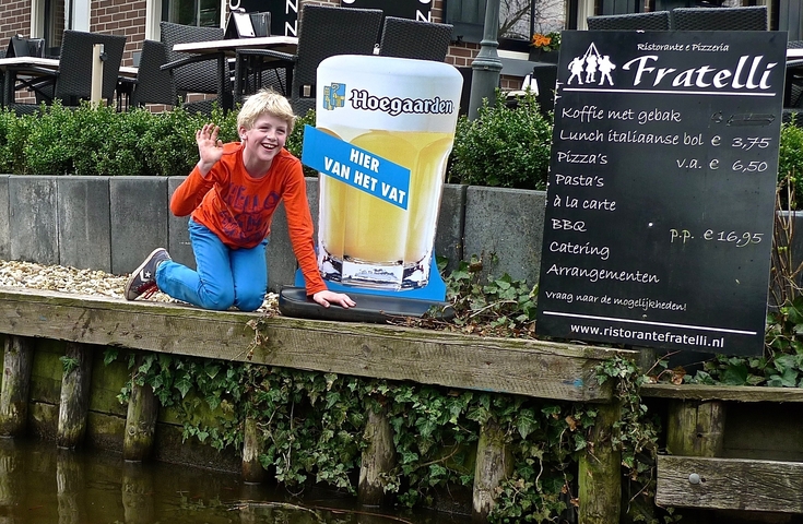 A person posing with a restaurant sign on a canal.