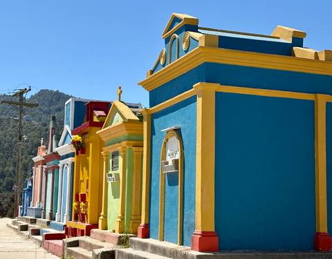       Row of brightly painted mausoleums in a sun-lit Guatemalan cemetery
  
