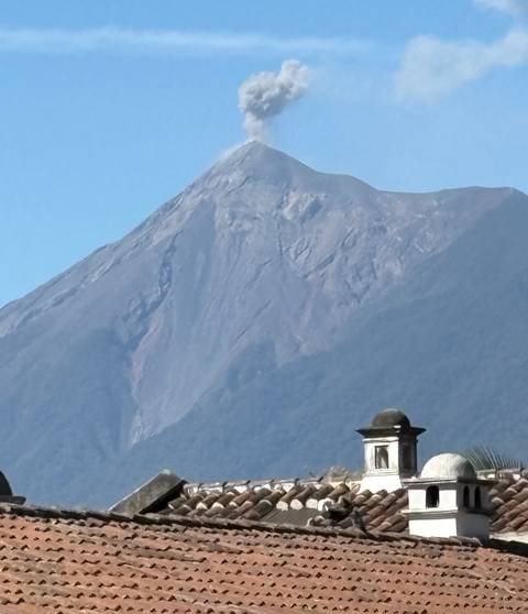       Historic rooftop with a looming volcano peak under clear blue sky
  