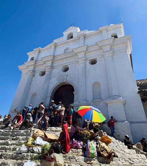       Locals gather on the steps of a white colonial church under a bright blue sky
  