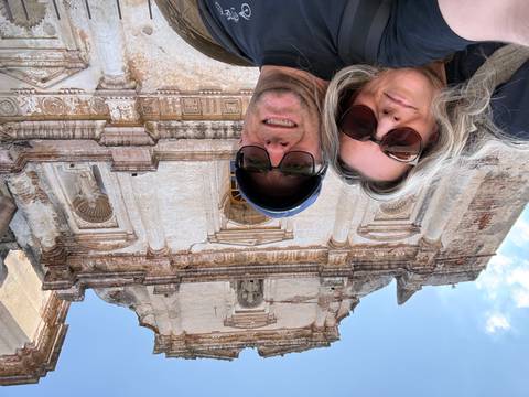       Couple taking a selfie beneath ornate colonial ruins with blue sky overhead
  