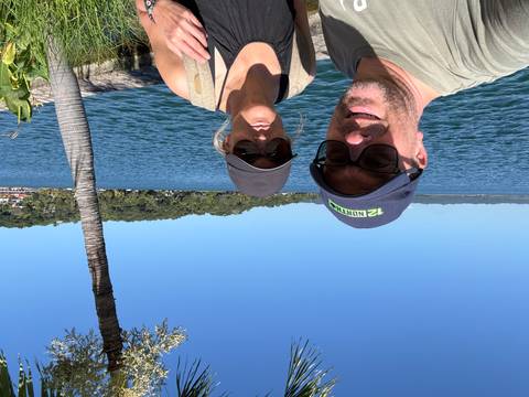      Couple posing by a lakeside promenade under clear skies with lush shore behind
  